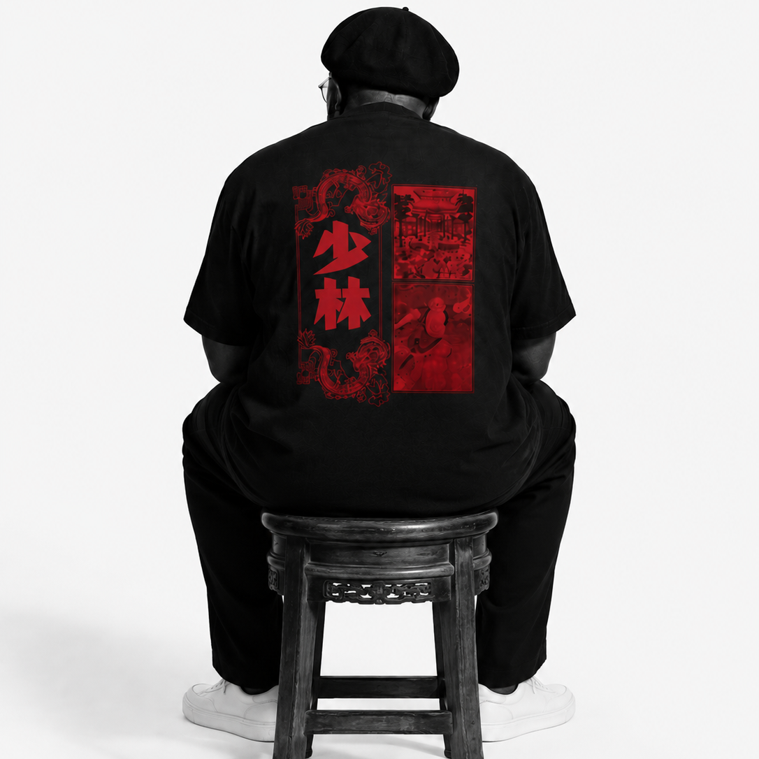 Person wearing a black t-shirt with red graphics sitting on a wooden stool against a white background